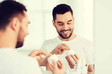 Image showing happy young man applying cream to face at bathroom