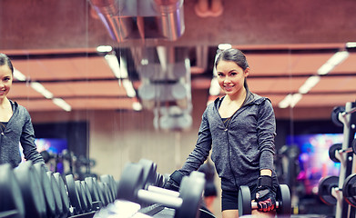 Image showing smiling young woman choosing dumbbells in gym