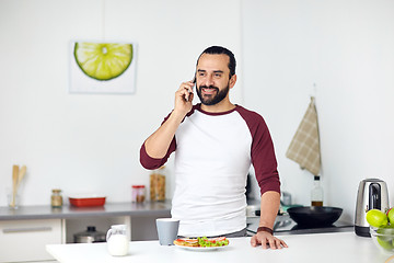 Image showing man calling on smartphone and eating at home