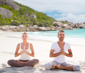 Image showing smiling couple making yoga exercises on beach