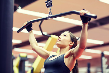 Image showing woman flexing arm muscles on cable machine in gym