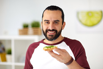 Image showing man eating avocado sandwiches at home kitchen