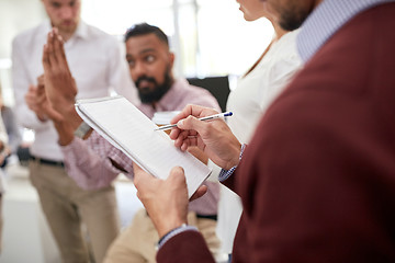 Image showing business team and man writing to notepad at office