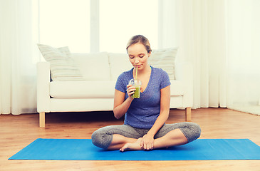 Image showing happy woman with smoothie sitting on mat at home