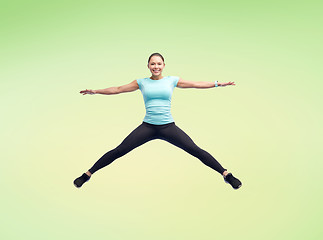 Image showing happy smiling sporty young woman jumping in air