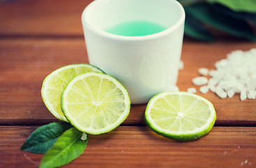 Image showing close up of body lotion in cup and limes on wood