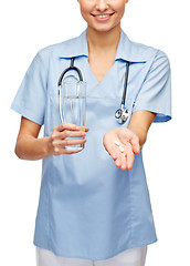 Image showing smiling doctor or nurse offering pills and water