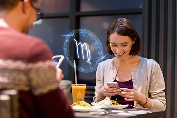 Image showing couple with smartphones and zodiac signs at cafe