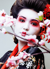 Image showing young pretty geisha in black kimono among sakura, asian ethno close up