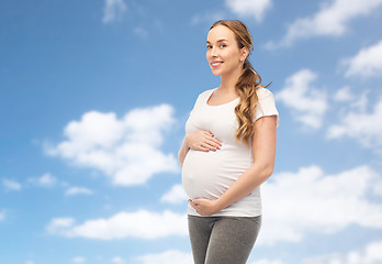 Image showing happy pregnant woman touching her belly over sky