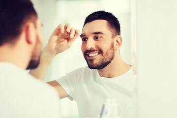 Image showing man with tweezers tweezing eyebrow at bathroom