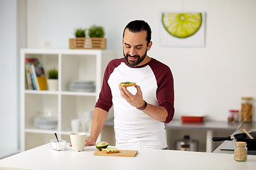 Image showing man eating avocado sandwiches at home kitchen