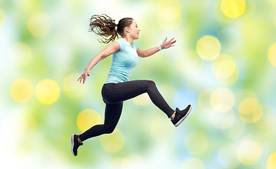 Image showing happy smiling sporty young woman jumping in air