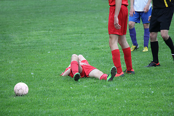 Image showing Injured player at the football match lying on the grass