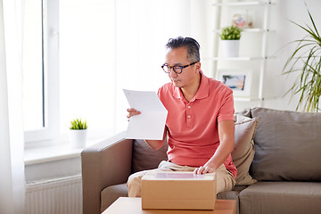 Image showing man with parcel box reading invoice at home