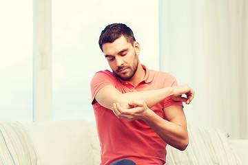 Image showing unhappy man suffering from pain in hand at home