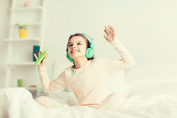 Image showing girl sitting on bed with smartphone and headphones