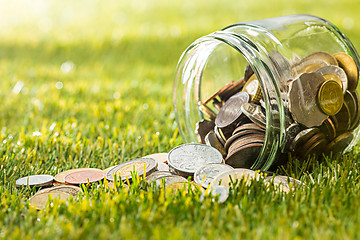 Image showing The coins at glass jar for money on green grass