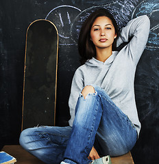 Image showing young cute teenage girl in classroom at blackboard seating on ta