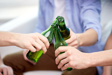 Image showing close up of friends clinking beer bottles at home