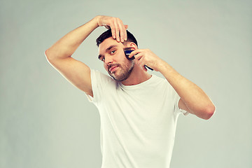 Image showing smiling man shaving beard with trimmer over gray