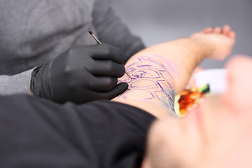 Image showing Tatoo drawing on his shoulder. Tattoo, tattoo artist does the tattoo on the man's hand.