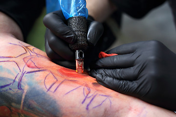 Image showing The tattoo parlor. A tattoo artist tattooing color tattoo on his hand man Tattooer tattooing color tattoo on his hand man