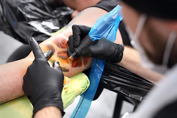 Image showing A man in a tattoo parlor. Tattoo, tattoo artist does the tattoo on the man's hand. Color tattoo.