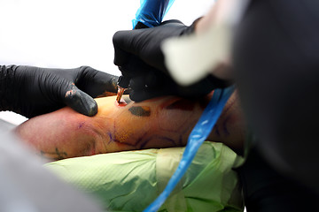 Image showing The tattoo parlor. A tattoo artist tattooing color tattoo on his hand man