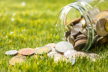 Image showing The coins at glass jar for money on green grass
