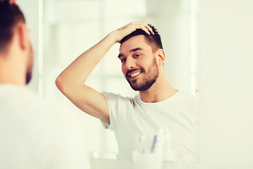 Image showing happy young man looking to mirror at home bathroom