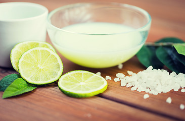 Image showing close up of body lotion in bowl and limes on wood