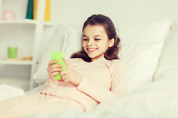 Image showing happy girl lying in bed with smartphone at home