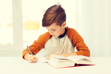 Image showing student boy with book writing to notebook at home