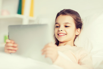 Image showing happy girl lying in bed with tablet pc at home