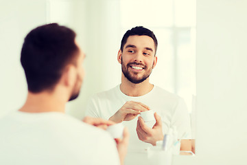 Image showing happy young man applying cream to face at bathroom