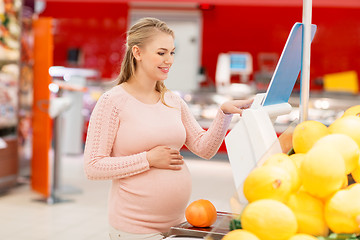 Image showing pregnant woman with grapefruit on scale at grocery