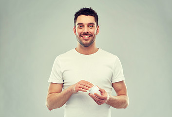 Image showing happy young man with cream jar over gray