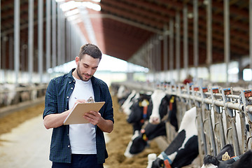 Image showing farmer with clipboard and cows in cowshed on farm