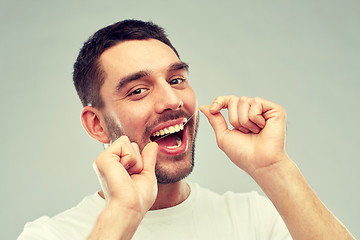 Image showing man with dental floss cleaning teeth over gray