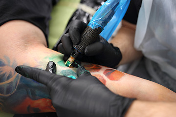 Image showing Tattoo, tattoo artist does the tattoo on the man's hand. Color tattoo. Tattoo Studio.