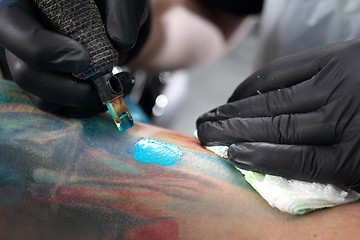 Image showing Color tattoo. The man in the tattoo parlor Tatoo. Tattoo artist fills the pattern in blue ink