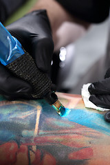 Image showing Color tattoo. The man in the tattoo parlor Tatoo. Tattoo artist fills the pattern in blue ink