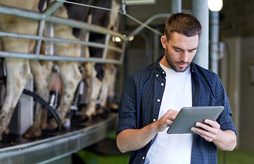 Image showing young man with tablet pc and cows on dairy farm