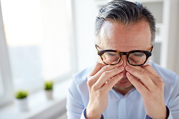 Image showing businessman in glasses rubbing eyes at office