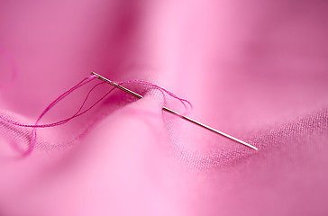 Image showing sewing needle with thread stuck into pink fabric