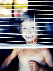 Image showing Little cute boy throught window making funny faces, home alone l