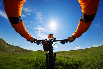 Image showing Hands in orange jacket holding handlebar of a bicycle