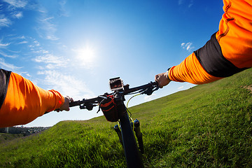 Image showing Hands in orange jacket holding handlebar of a bicycle