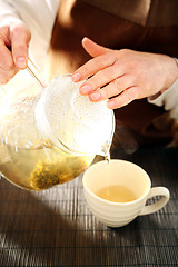 Image showing Blooming tea brewed in a glass jug. Blooming tea. The waitress pours tea into a cup